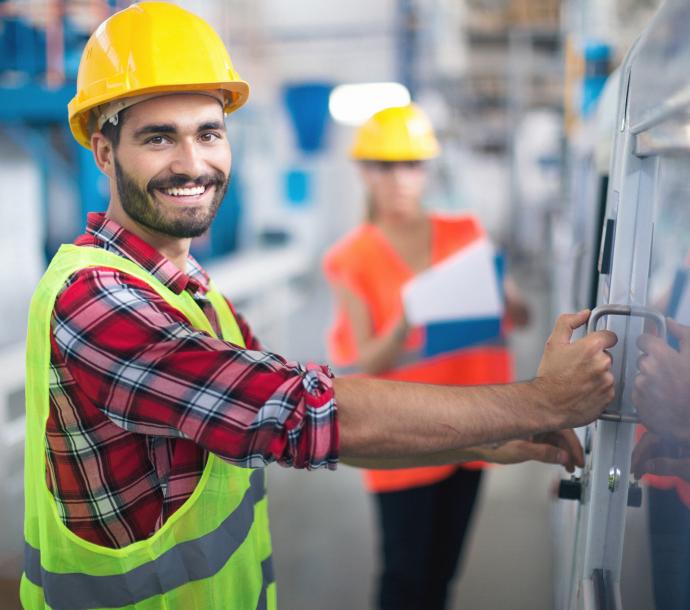 Mann im Bauhelm bedient Schaltkasten im Werk