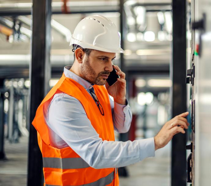 Arbeiter im Helm bedient ein Bedienfeld im Industriegebäude