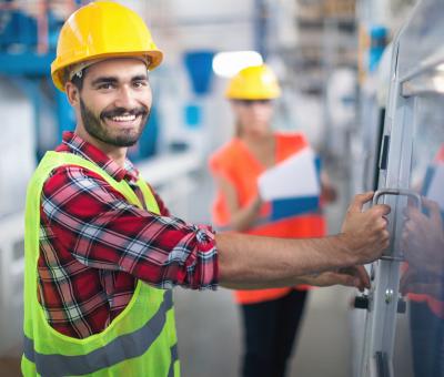 Mann im Bauhelm bedient Schaltkasten im Werk