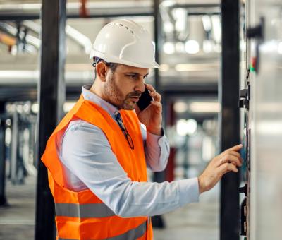 Arbeiter im Helm bedient ein Bedienfeld im Industriegebäude